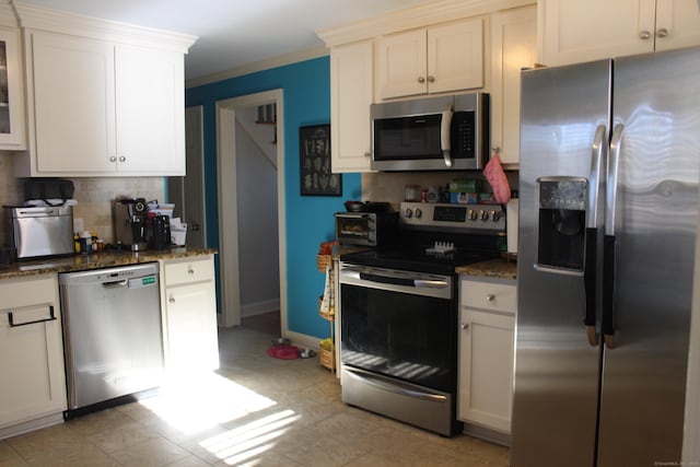 kitchen featuring white cabinetry, dark stone countertops, decorative backsplash, stainless steel appliances, and crown molding