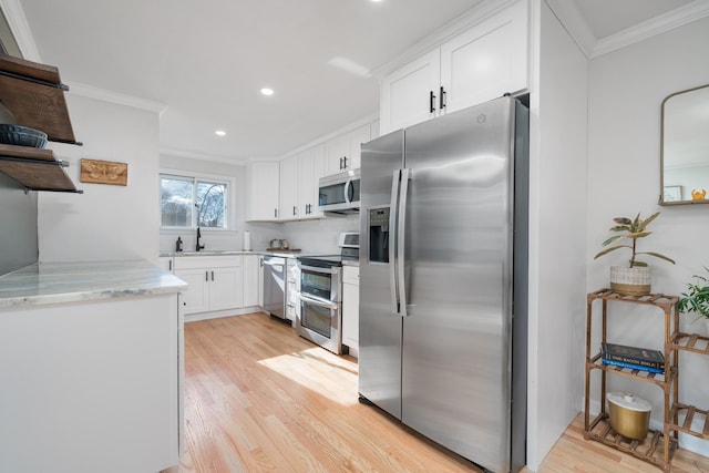 kitchen with sink, crown molding, appliances with stainless steel finishes, white cabinetry, and light stone countertops