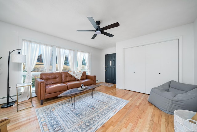 living room featuring ceiling fan, a baseboard heating unit, and light wood-type flooring