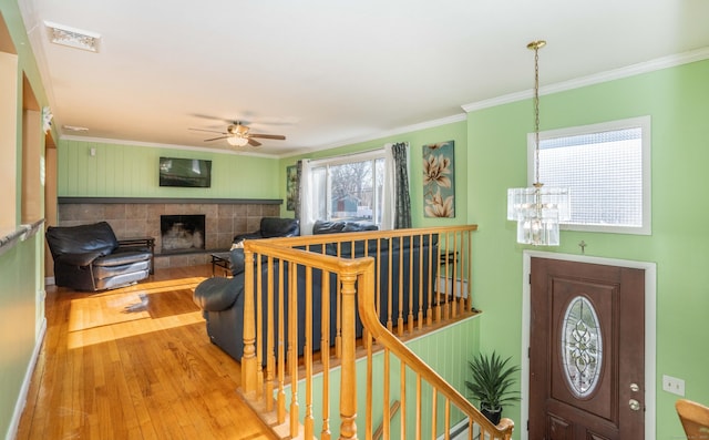 foyer entrance featuring hardwood / wood-style flooring, ornamental molding, ceiling fan with notable chandelier, and a fireplace