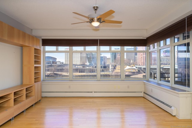 unfurnished sunroom featuring a baseboard radiator, a view of city, and a ceiling fan