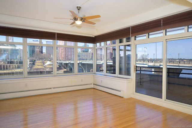 unfurnished sunroom with a city view, baseboard heating, and ceiling fan