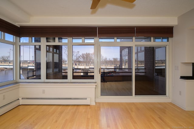 unfurnished sunroom with a ceiling fan and a baseboard radiator