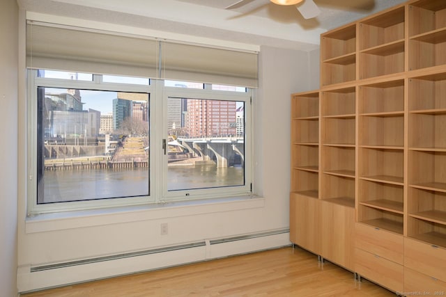 spare room with a wealth of natural light, a view of city, light wood-style floors, and a baseboard radiator