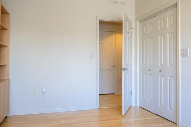 unfurnished bedroom with light wood-type flooring, baseboards, and a closet