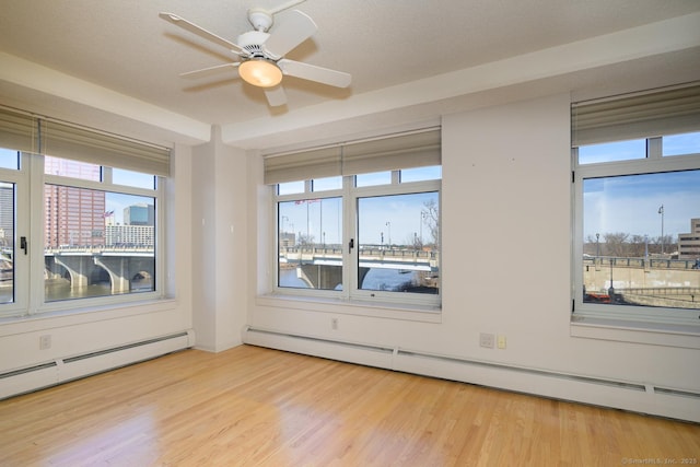 spare room with a baseboard heating unit, plenty of natural light, wood finished floors, and a baseboard radiator