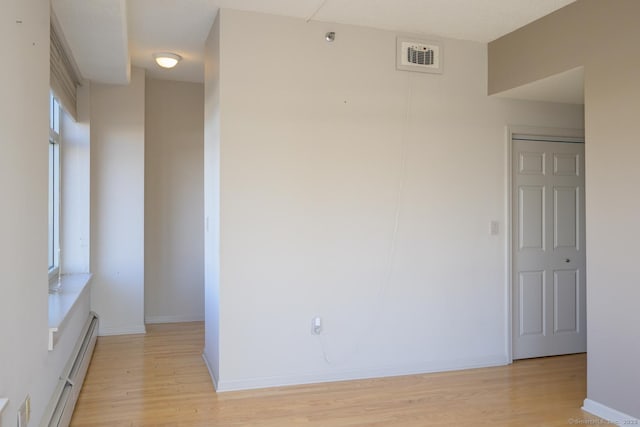 empty room featuring a baseboard heating unit, visible vents, light wood-type flooring, and baseboards