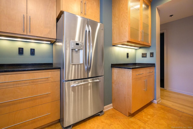 kitchen featuring glass insert cabinets, stainless steel fridge, baseboards, and brown cabinetry