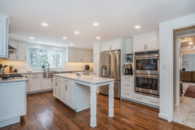 kitchen with sink, white cabinets, a center island, stainless steel appliances, and wall chimney range hood