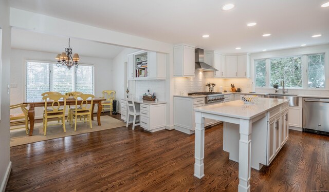 kitchen featuring white cabinetry, appliances with stainless steel finishes, hanging light fixtures, and wall chimney range hood