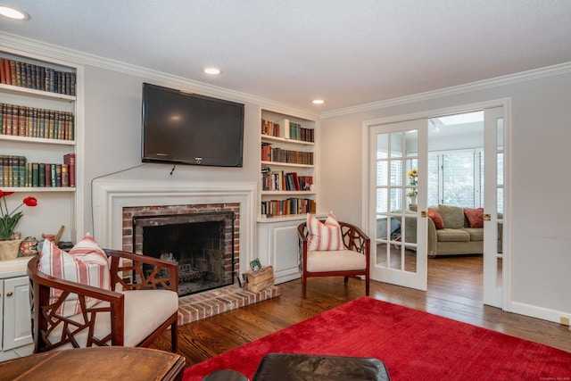 living area featuring dark hardwood / wood-style flooring, built in shelves, a fireplace, and ornamental molding