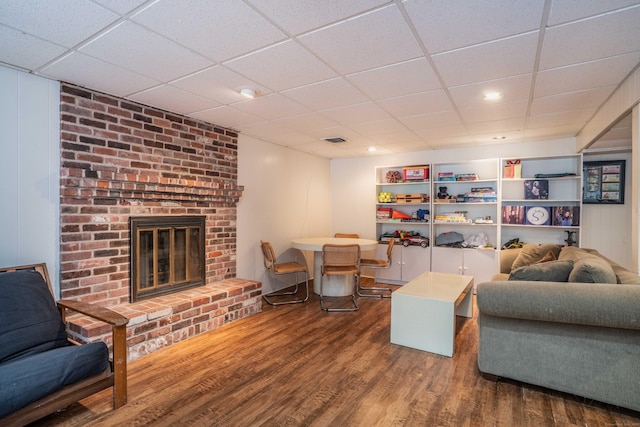 living room featuring a drop ceiling, hardwood / wood-style flooring, and a fireplace