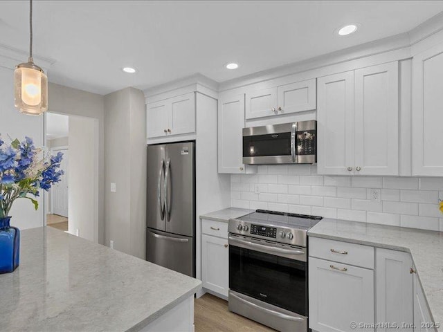 kitchen with hanging light fixtures, backsplash, stainless steel appliances, light stone counters, and white cabinets