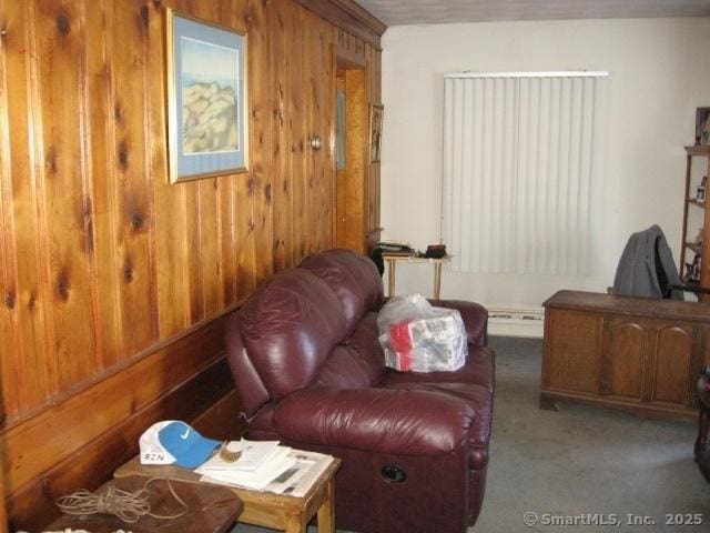 living area with a baseboard heating unit, wooden walls, and carpet