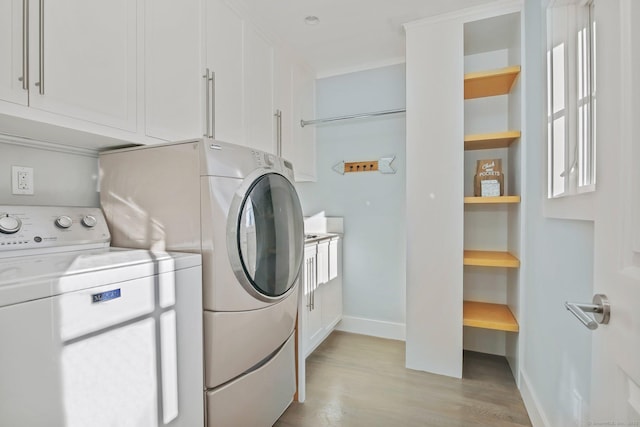 clothes washing area with washer and clothes dryer, cabinets, and light wood-type flooring