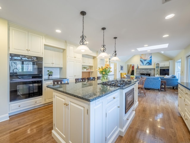 kitchen with a stone fireplace, lofted ceiling with skylight, a center island, double oven, and pendant lighting