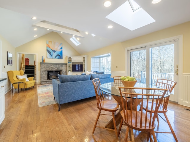 dining area with a stone fireplace, vaulted ceiling with skylight, and light wood-type flooring