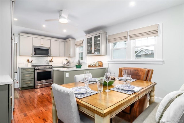 kitchen featuring gray cabinets, ceiling fan, stainless steel appliances, hardwood / wood-style floors, and backsplash