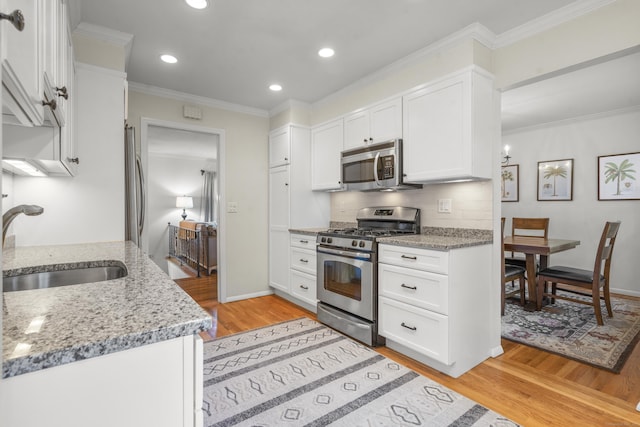 kitchen with white cabinetry, sink, ornamental molding, light stone counters, and stainless steel appliances