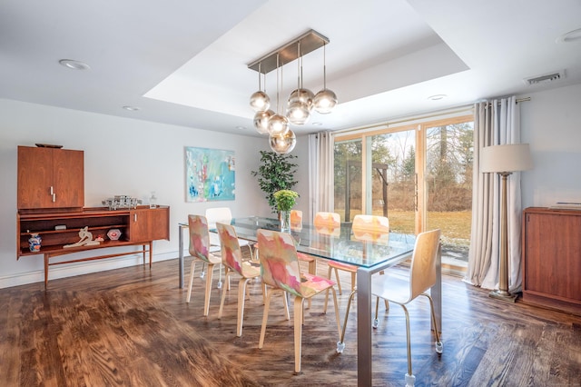 dining area featuring dark wood-type flooring, a chandelier, and a tray ceiling