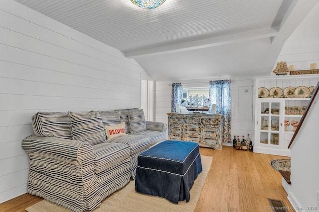 living room featuring wood walls, lofted ceiling with beams, and light wood-type flooring