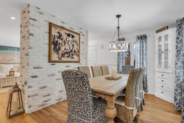 dining space with brick wall and light wood-type flooring