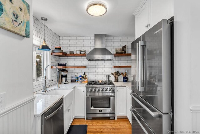 kitchen with sink, white cabinetry, premium appliances, decorative light fixtures, and wall chimney exhaust hood