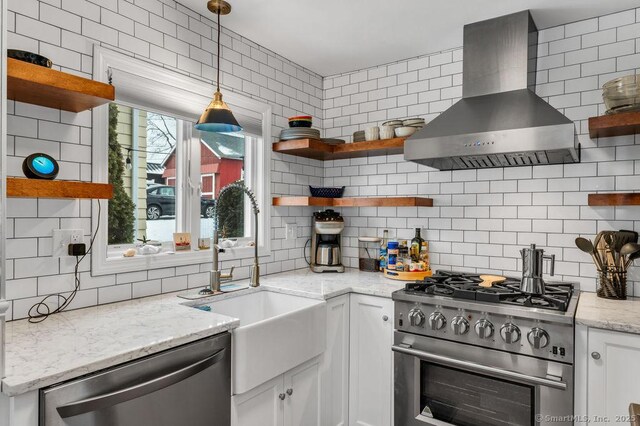 kitchen with wall chimney range hood, sink, appliances with stainless steel finishes, white cabinetry, and light stone countertops