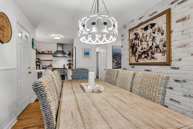 dining space with hardwood / wood-style flooring, brick wall, and a chandelier