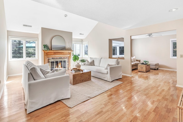 living room with a fireplace, light hardwood / wood-style flooring, ceiling fan, and vaulted ceiling