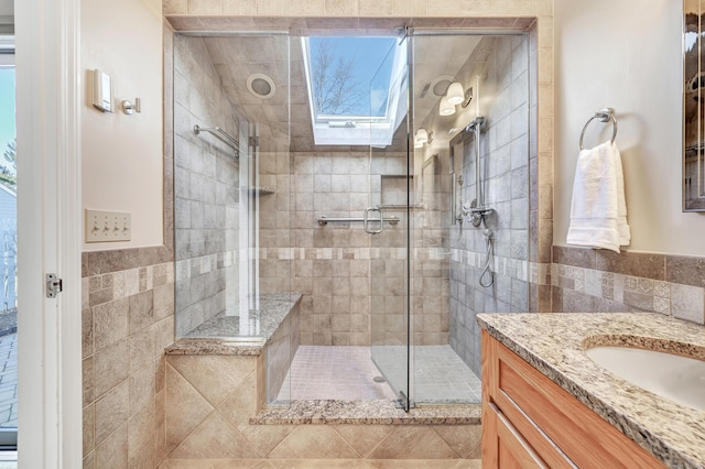 bathroom with vanity, a skylight, a shower with door, and tile walls