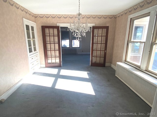 unfurnished dining area with radiator, french doors, and a chandelier