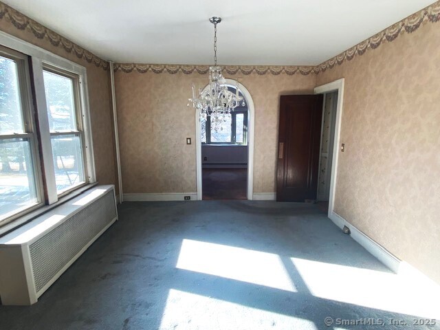 unfurnished dining area featuring an inviting chandelier, radiator heating unit, and dark colored carpet