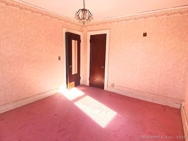 carpeted spare room with crown molding and an inviting chandelier