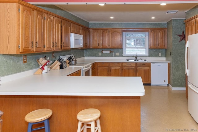 kitchen with white appliances, a kitchen bar, kitchen peninsula, and sink