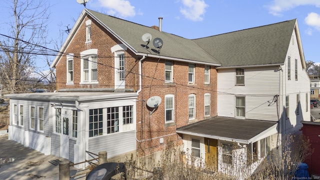 rear view of house featuring brick siding and roof with shingles