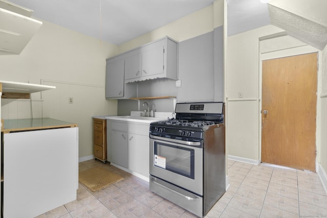 kitchen with stainless steel gas range oven, gray cabinets, vaulted ceiling, light countertops, and a sink