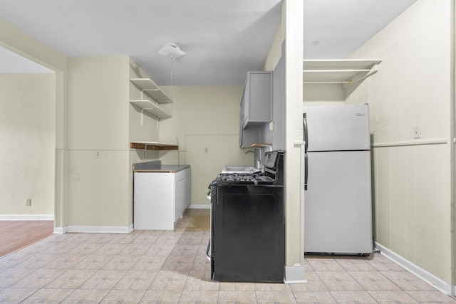 kitchen with a wainscoted wall, a sink, freestanding refrigerator, washer / clothes dryer, and gas range oven