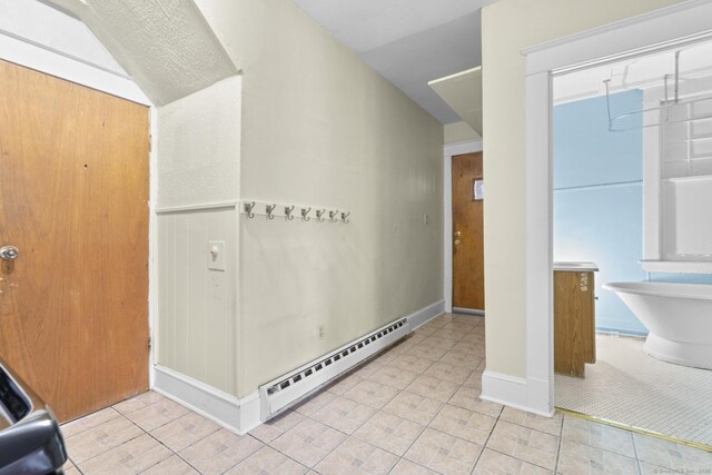 interior space with wainscoting, vaulted ceiling, baseboard heating, and light tile patterned floors