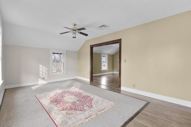 spare room with wood finished floors, a ceiling fan, visible vents, vaulted ceiling, and baseboards