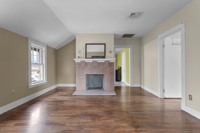 unfurnished living room with dark wood-style floors, vaulted ceiling, a fireplace, and visible vents