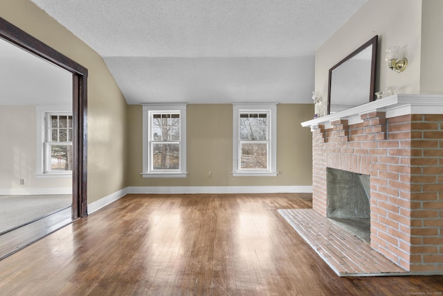 unfurnished living room with lofted ceiling, a textured ceiling, a brick fireplace, and wood finished floors