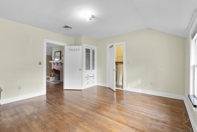 unfurnished living room with vaulted ceiling, a fireplace, wood finished floors, and baseboards