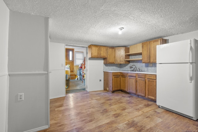 kitchen featuring brown cabinets, light wood finished floors, light countertops, freestanding refrigerator, and a sink