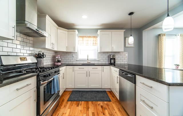 kitchen featuring white cabinetry, hanging light fixtures, wall chimney exhaust hood, and appliances with stainless steel finishes