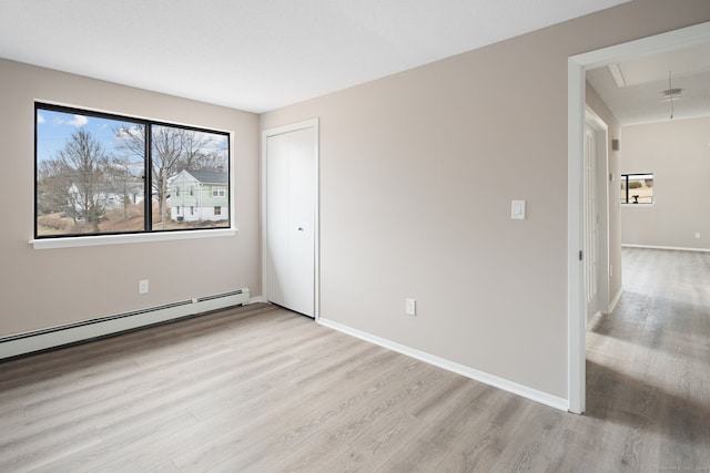 unfurnished bedroom featuring light wood-type flooring, a closet, a baseboard radiator, baseboards, and attic access