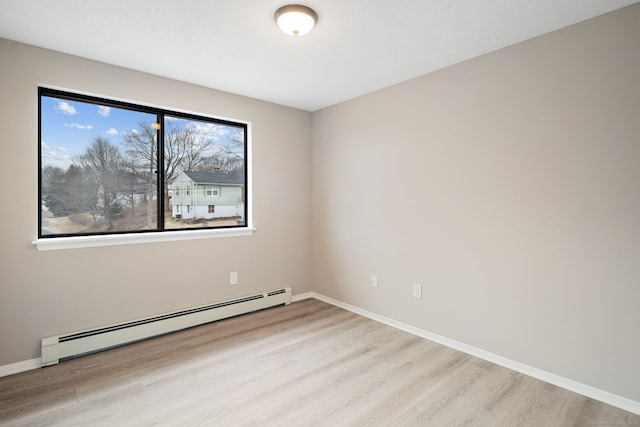 unfurnished room with a baseboard heating unit, baseboards, and light wood-style floors