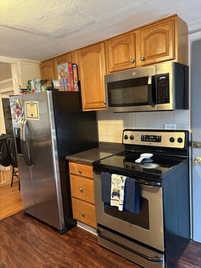 kitchen with appliances with stainless steel finishes, dark hardwood / wood-style floors, a textured ceiling, and backsplash