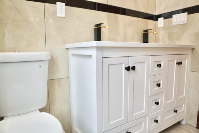 bathroom with vanity, toilet, and tile walls