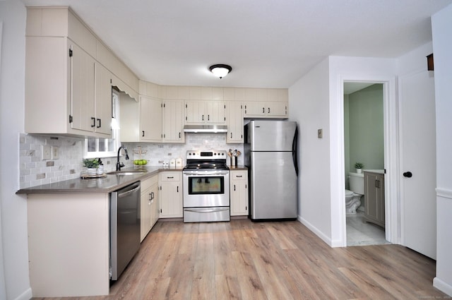 kitchen with appliances with stainless steel finishes, light hardwood / wood-style floors, sink, and backsplash